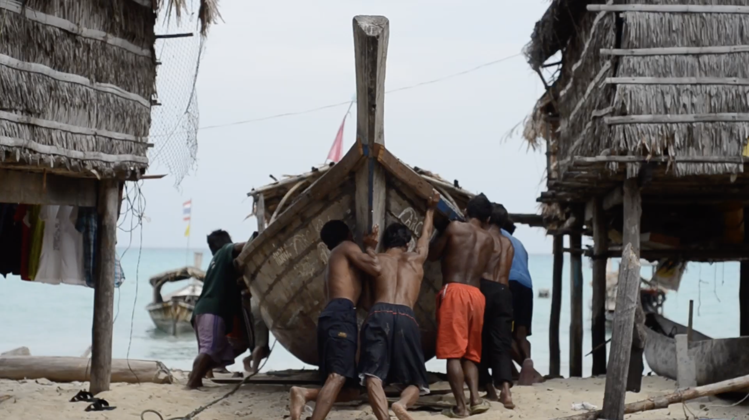 A group of men working together to push a wooden boat on a sandy beach.